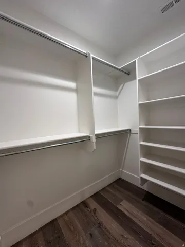 Walk-in closet featuring white built-in shelving, multiple hanging rods, and wood-finish flooring