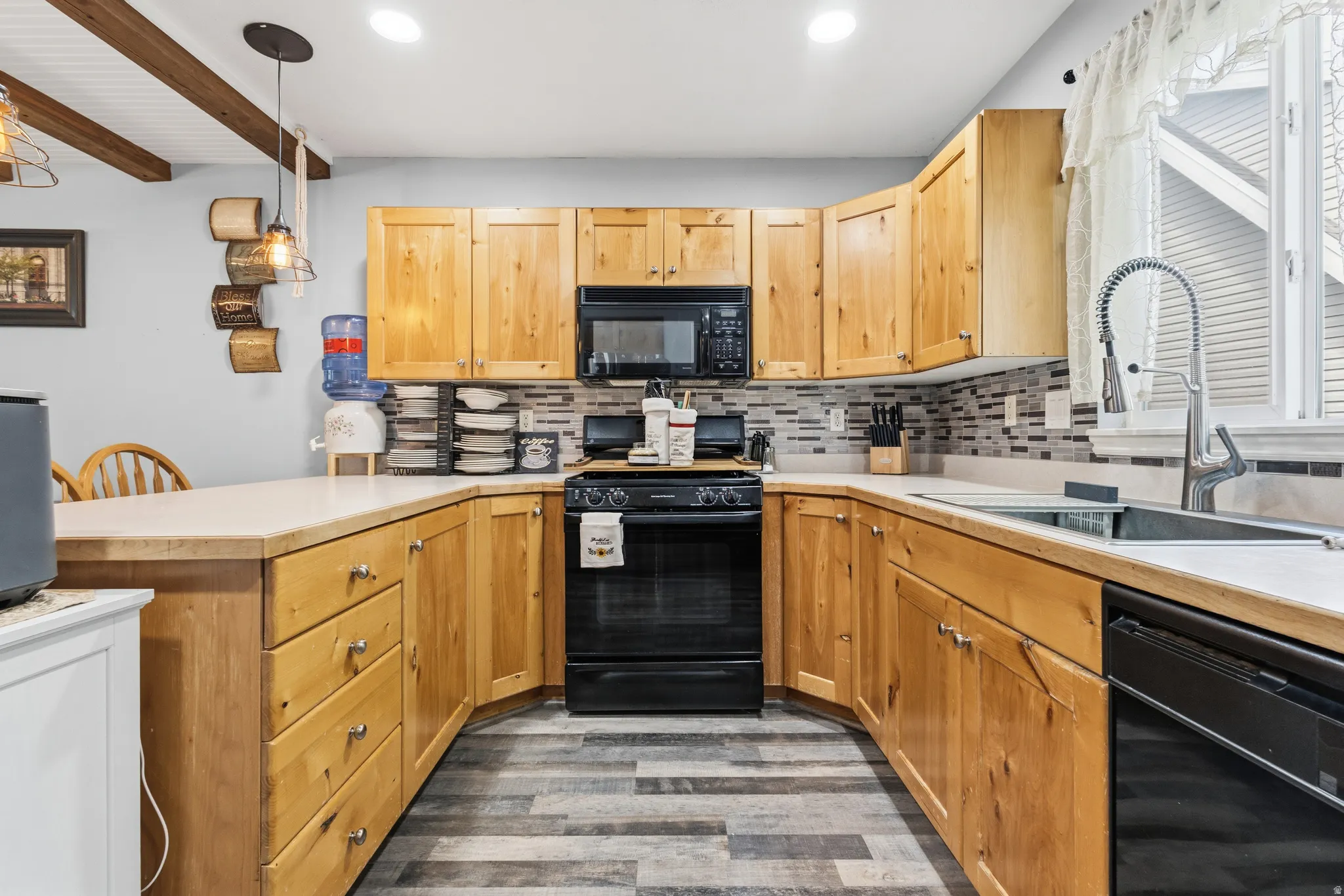U-shaped kitchen featuring light wood cabinetry, black appliances, a tile backsplash, and wood-finish flooring