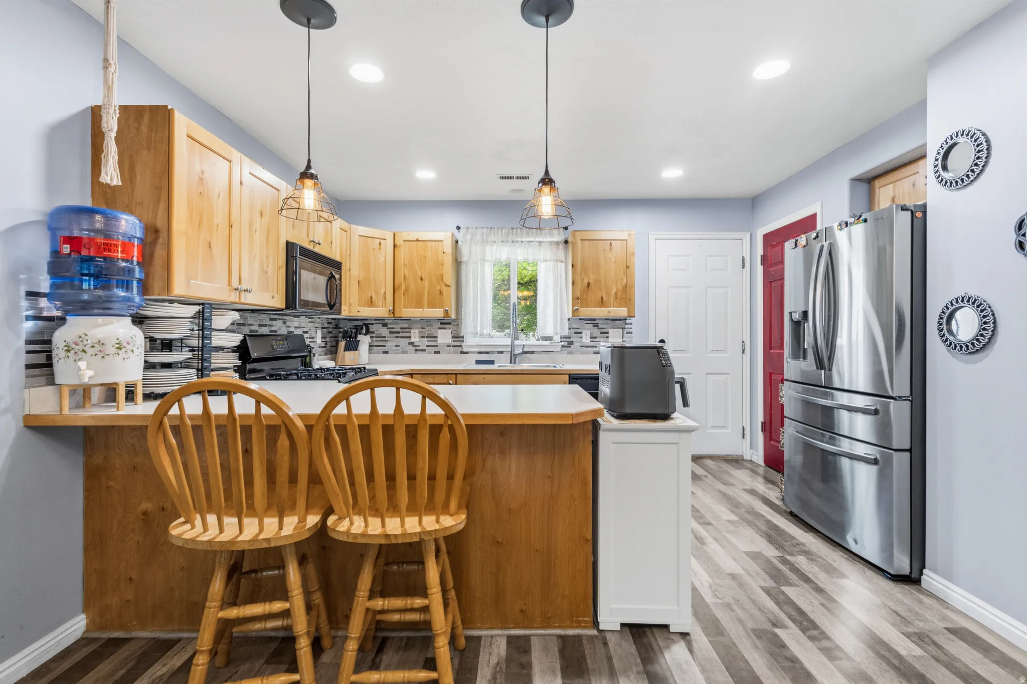 Kitchen featuring wood-finish cabinetry, white countertops, a tiled backsplash, stainless steel refrigerator, and wood-finish flooring