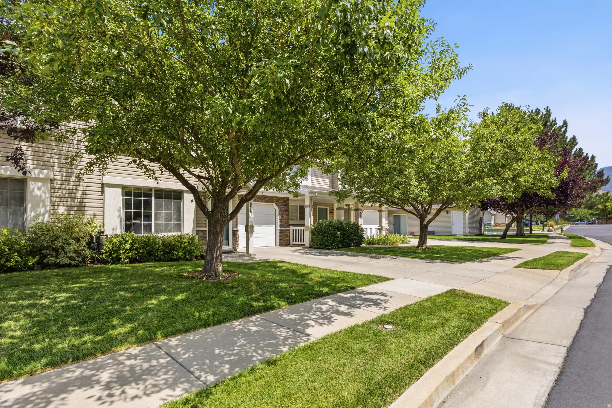 Siding exterior with stone accents, mature trees, manicured lawns, and concrete sidewalks