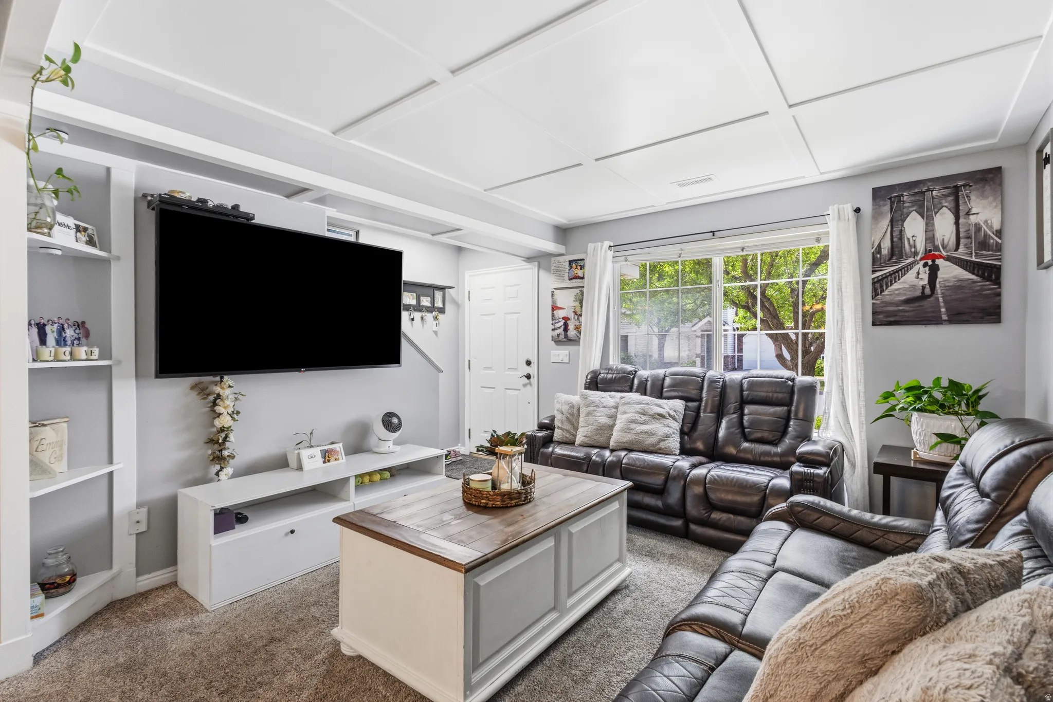 Spacious living area featuring light gray walls, plush carpet flooring, and a white coffered ceiling