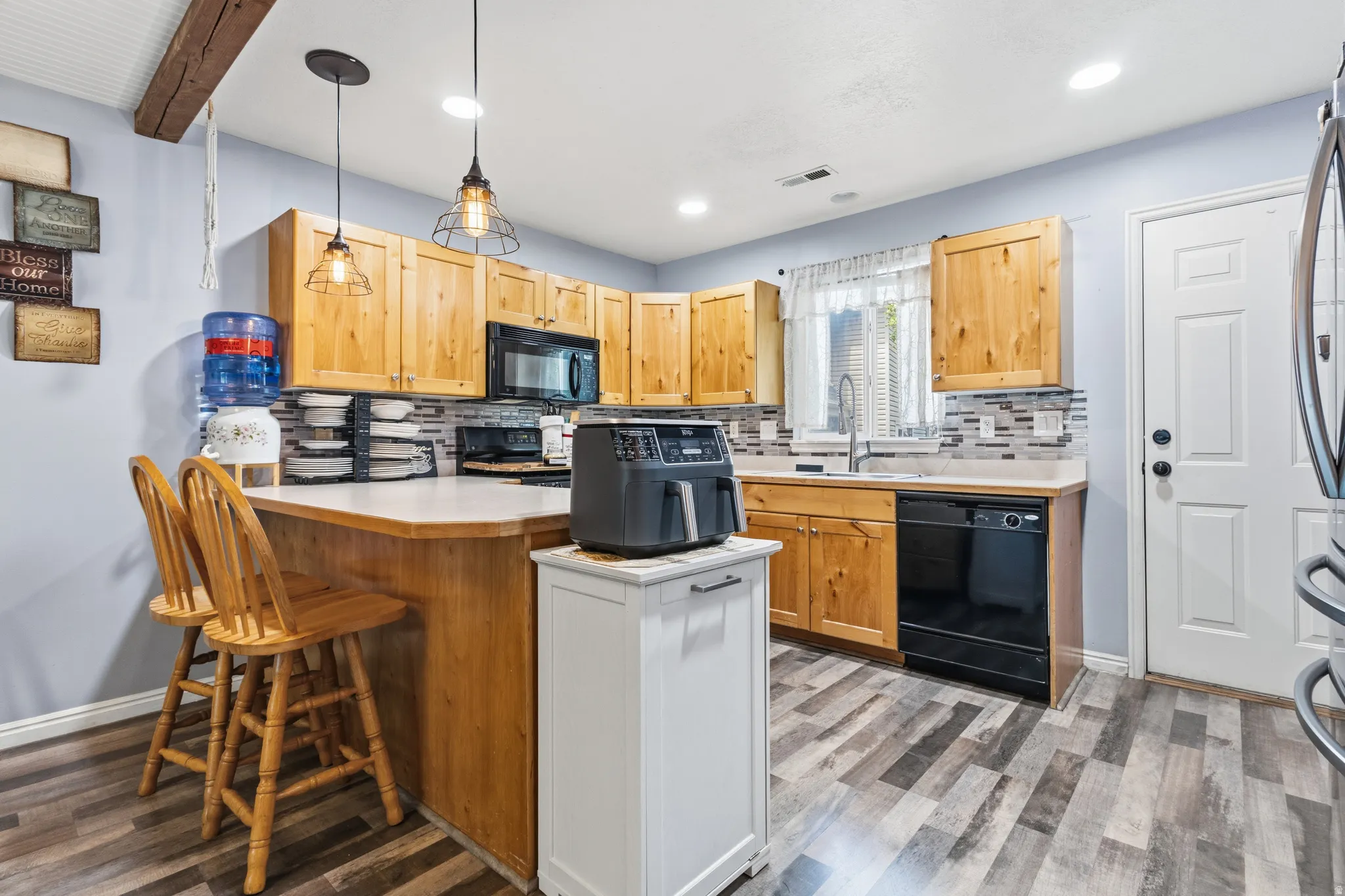 Kitchen featuring wood-finish flooring, natural wood cabinetry, light countertops, and a tiled backsplash
