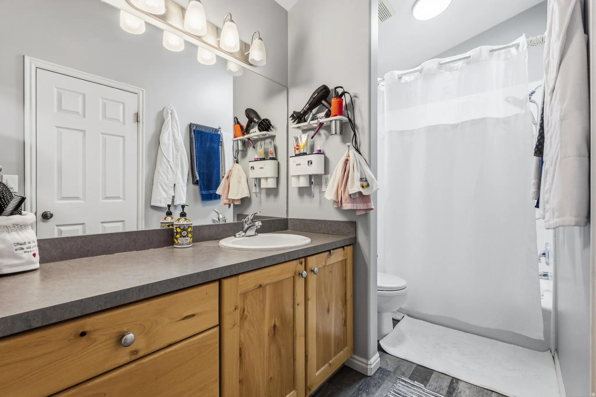 Bathroom featuring a light wood vanity with a dark countertop, an integrated sink, and a wall-mounted light fixture