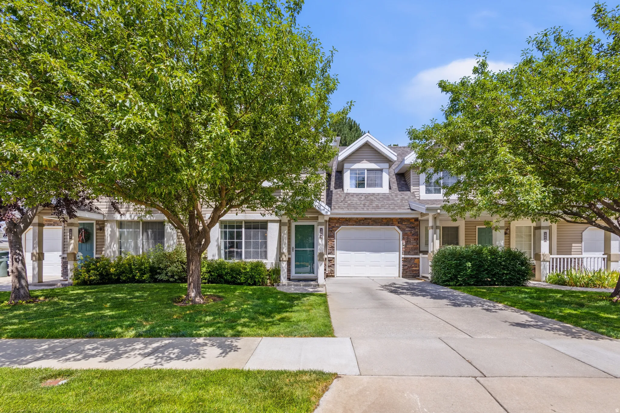 Two-story residence featuring dormer windows, stone accent siding, an attached garage, a private driveway, and a front porch with white railings