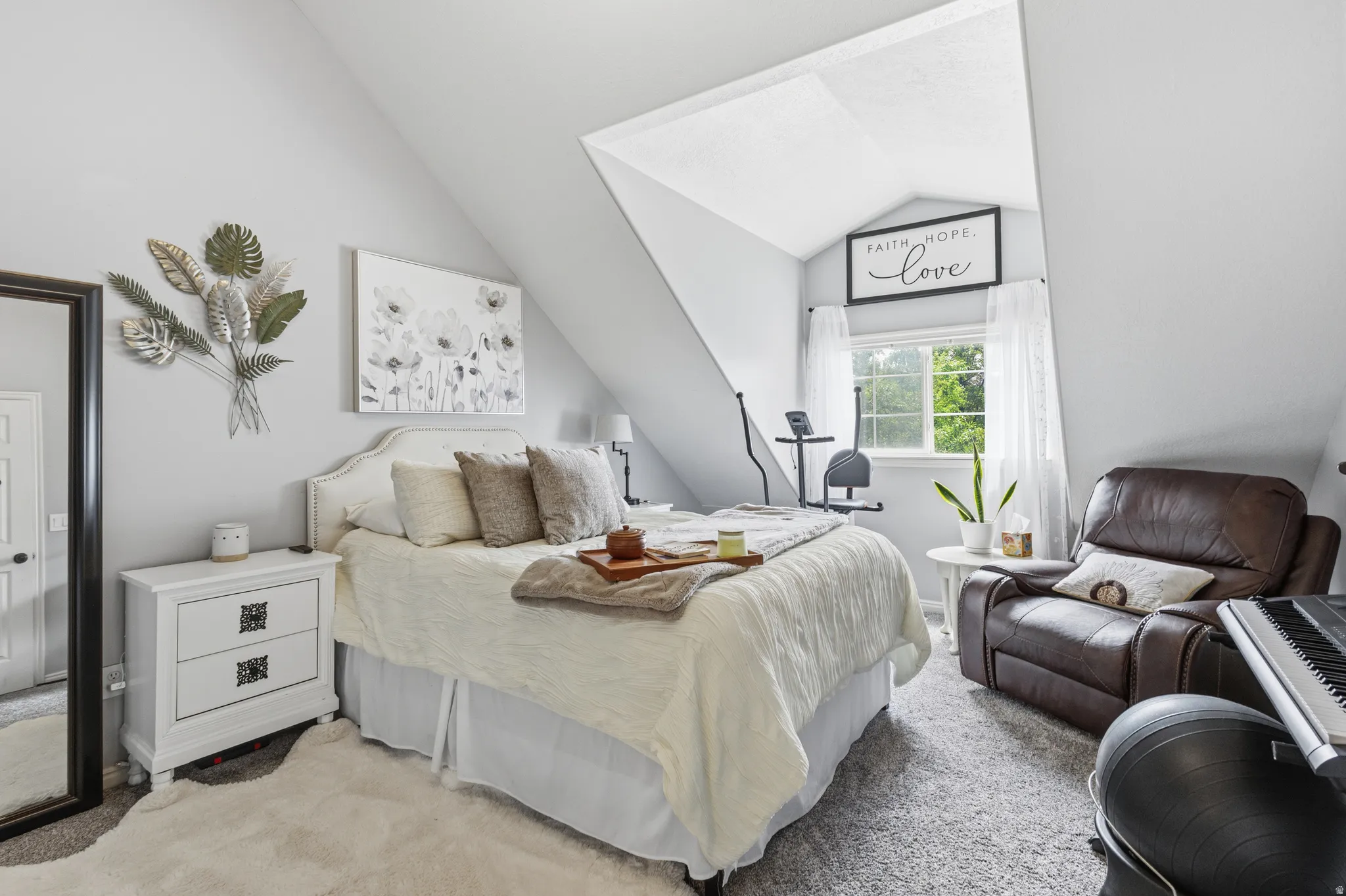 Sloped ceiling bedroom featuring a window with white curtains, light gray walls, and carpet flooring