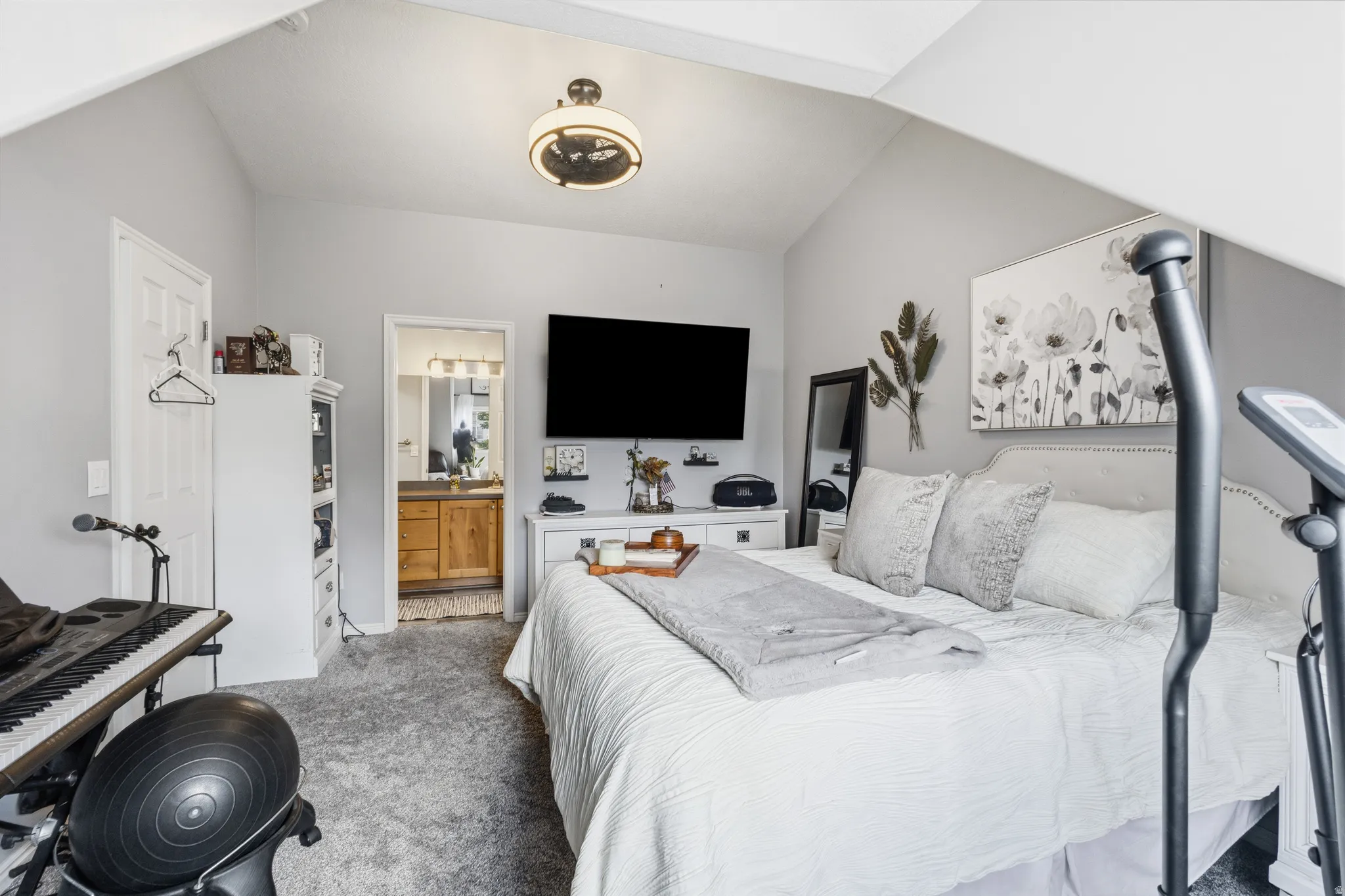 Bedroom featuring vaulted ceilings, plush carpeting, an en-suite bathroom entrance, a built-in light fixture, and light gray wall paint