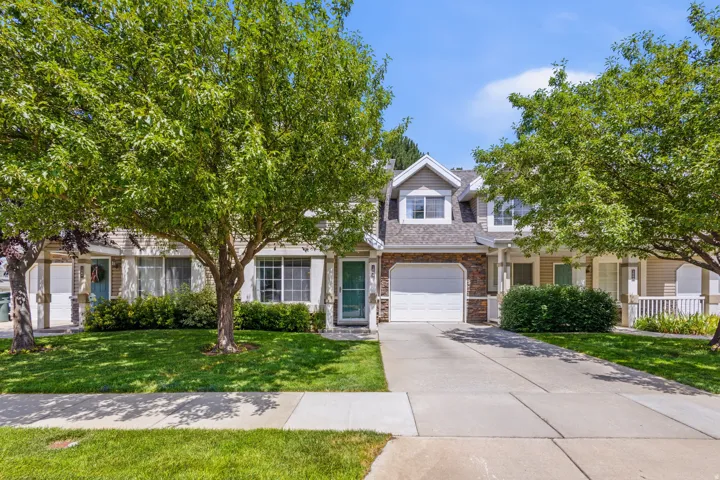Two-story residence featuring dormer windows, stone accent siding, an attached garage, a private driveway, and a front porch with white railings