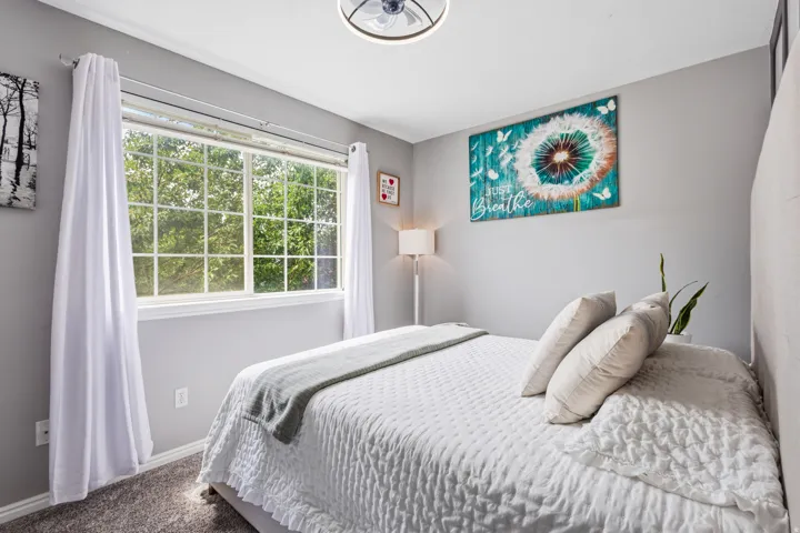 Room featuring gray wall paint, a large window with grid panes, textured carpet flooring, and a ceiling fan with integrated lighting