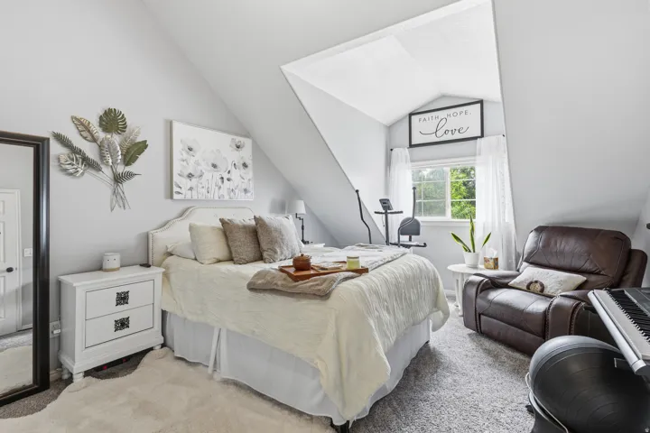 Sloped ceiling bedroom featuring a window with white curtains, light gray walls, and carpet flooring