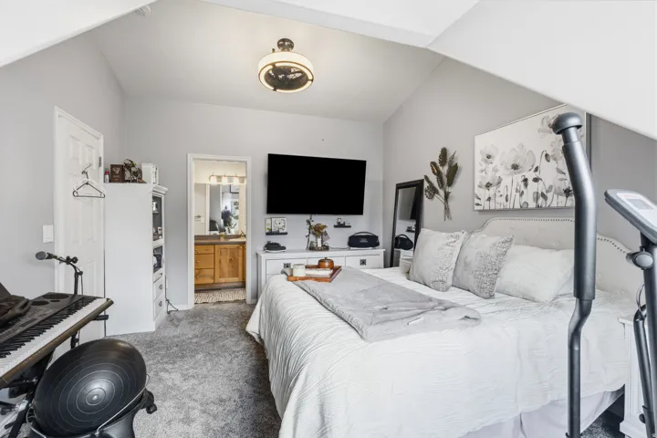 Bedroom featuring vaulted ceilings, plush carpeting, an en-suite bathroom entrance, a built-in light fixture, and light gray wall paint