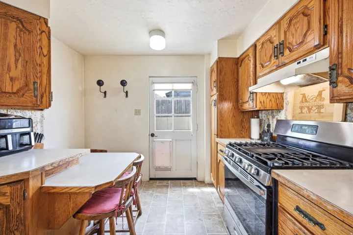 Kitchen featuring wood cabinetry, light-toned countertops, a stainless steel gas range with overhead ventilation, and durable tile flooring