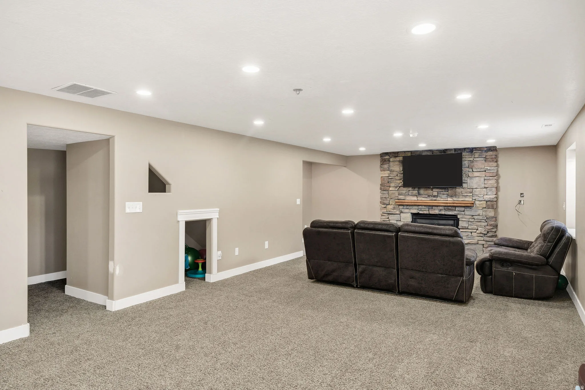 Spacious room featuring neutral carpeting, recessed lighting, and a stone-clad fireplace with a wood mantle