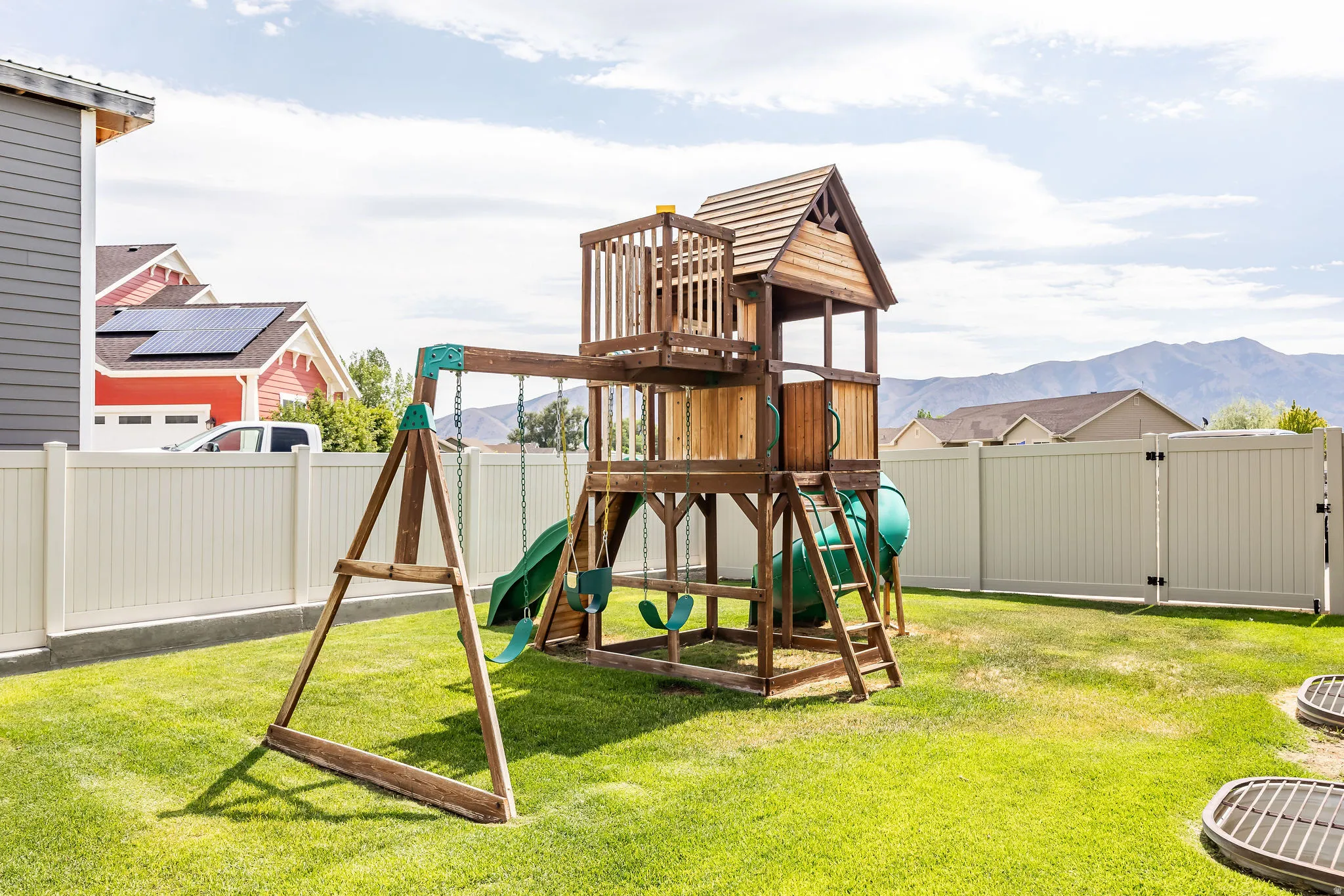 Expansive backyard featuring a manicured lawn, a wooden playset with swings and slides, and a full privacy fence