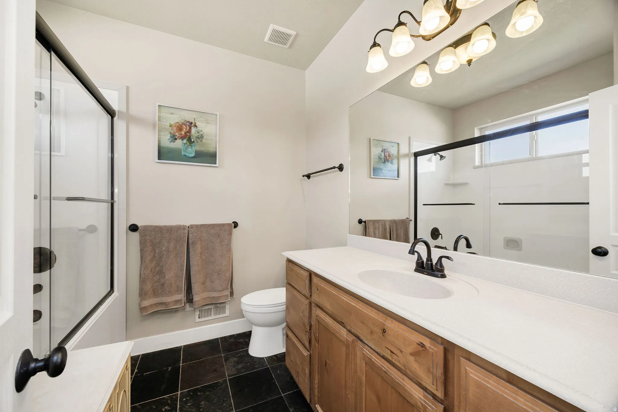 Bathroom featuring a wood-finish vanity with a white countertop, an integrated sink, and a dark bronze faucet