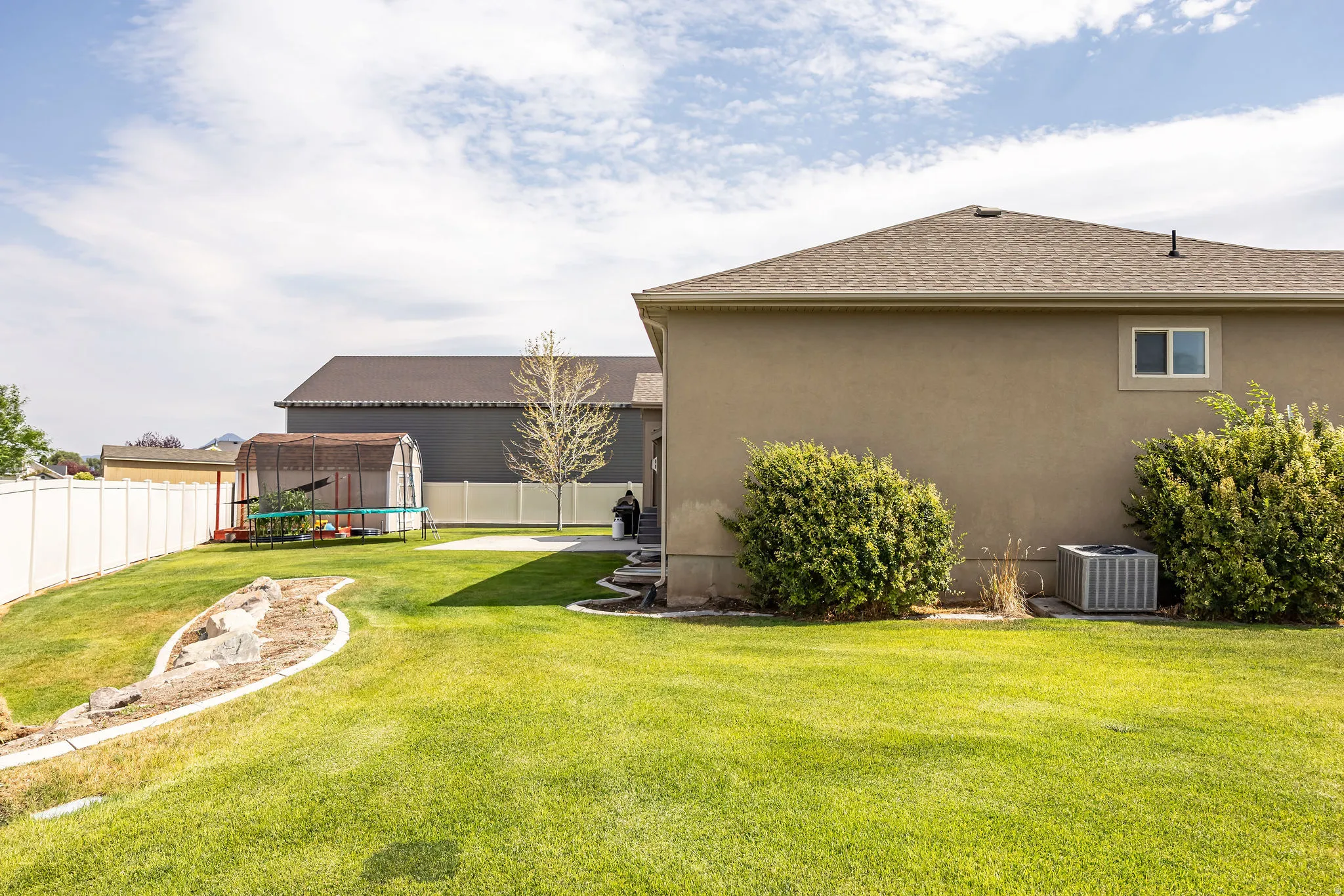 Expansive backyard with a manicured lawn, white vinyl fencing, and a decorative rock garden feature