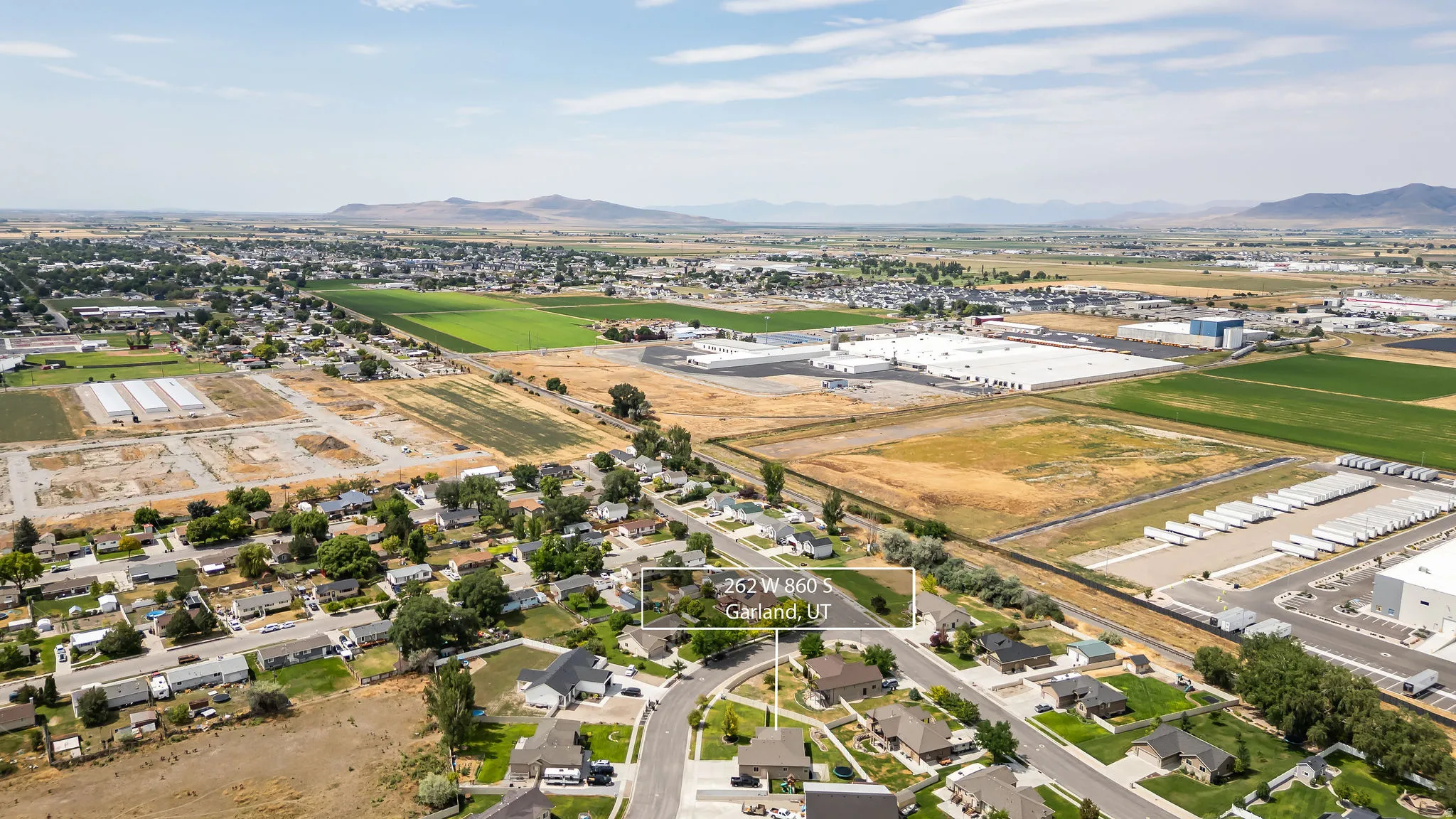 Aerial perspective of a residential street with single-family homes, surrounded by agricultural fields and commercial structures