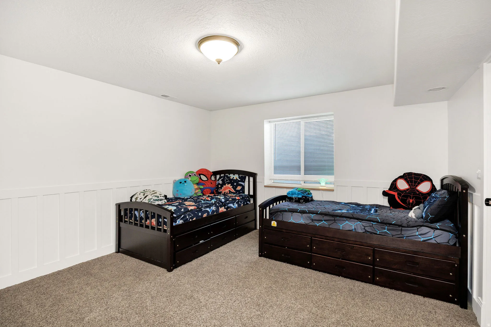 Spacious room featuring neutral carpet flooring, white walls with wainscoting, and a single window offering natural light