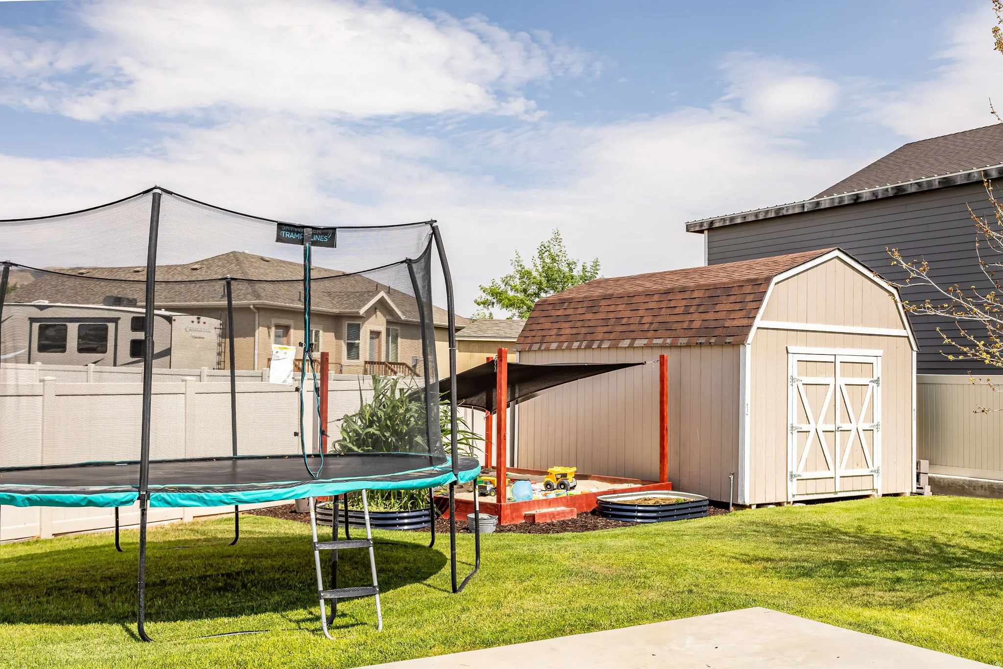 Expansive backyard featuring a spacious lawn, a charming storage shed with double barn doors and a shingled roof, a sandpit with a protective covering, and a privacy fence