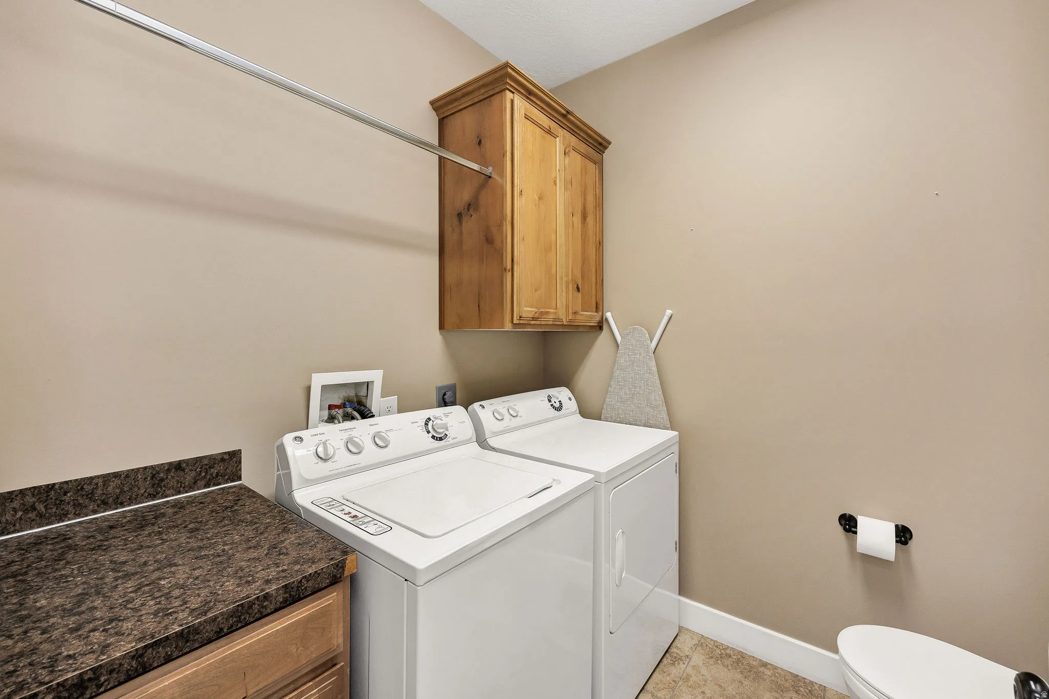 Dedicated laundry area featuring a wood-finish upper cabinet, a horizontal hanging rod, and a speckled dark countertop