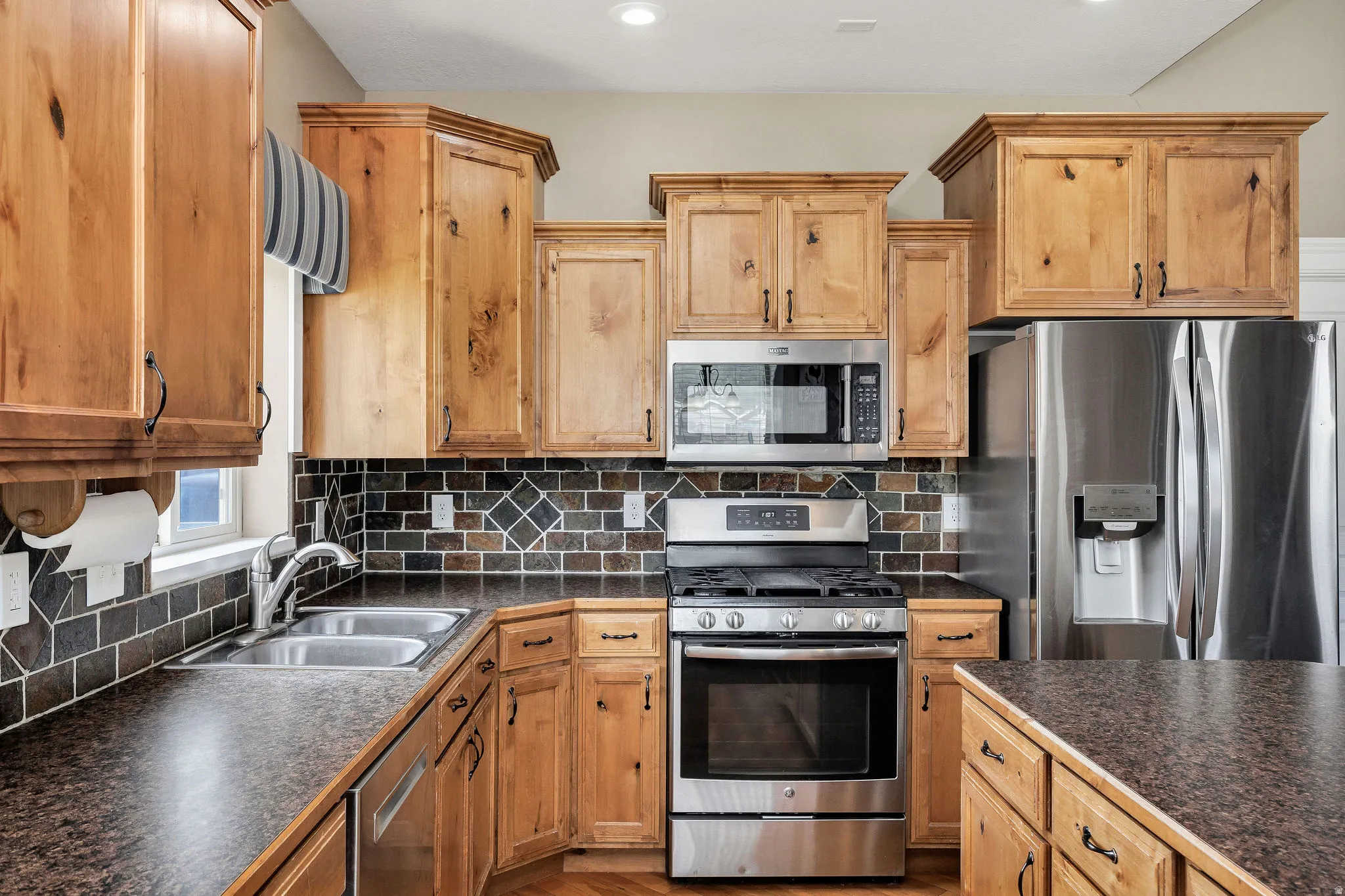 Kitchen featuring stainless steel appliances, wood cabinetry, dark countertops, and a tiled backsplash