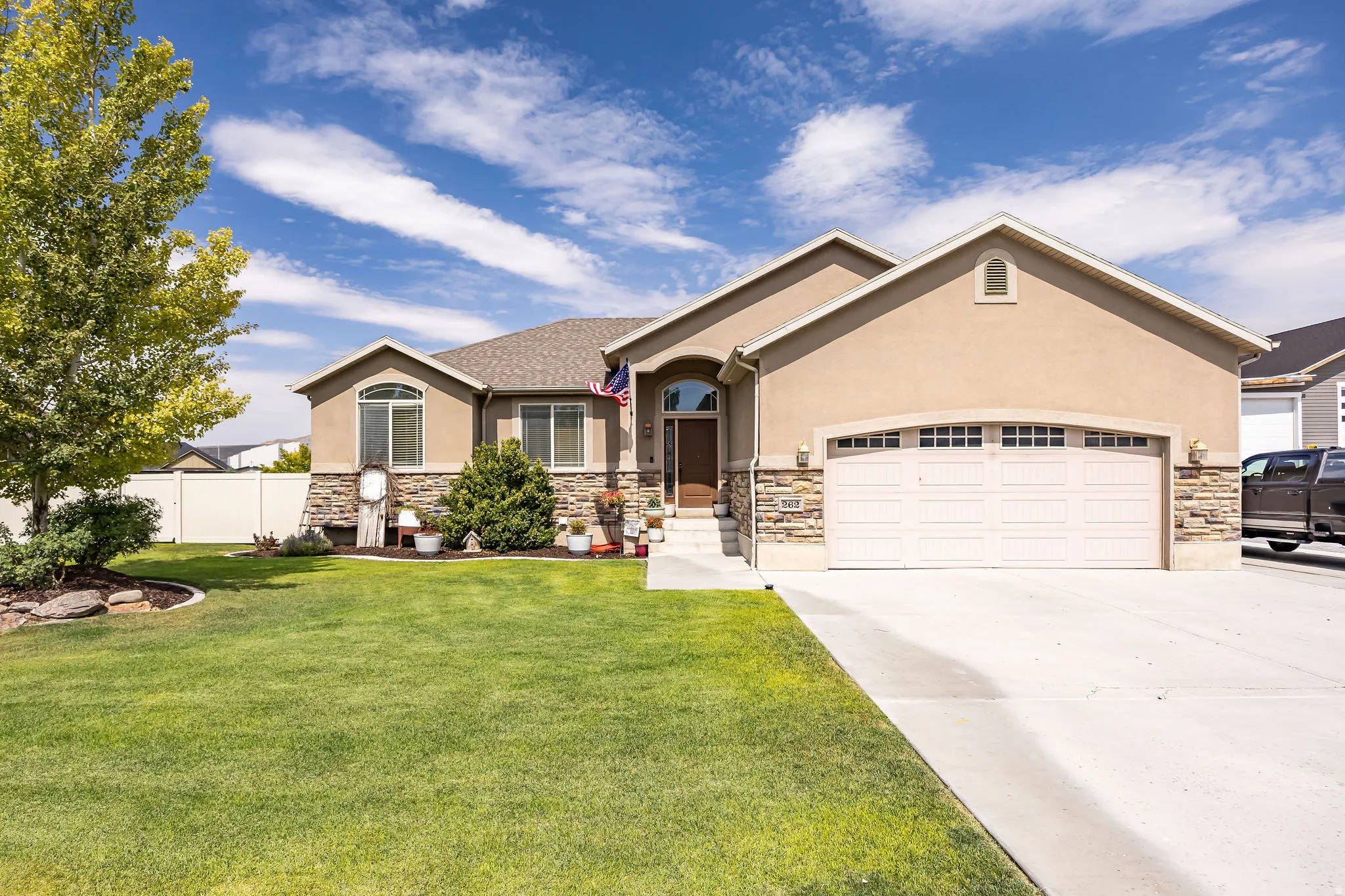 Contemporary stucco and stone-accented home featuring a two-car garage, concrete driveway, and a manicured front lawn