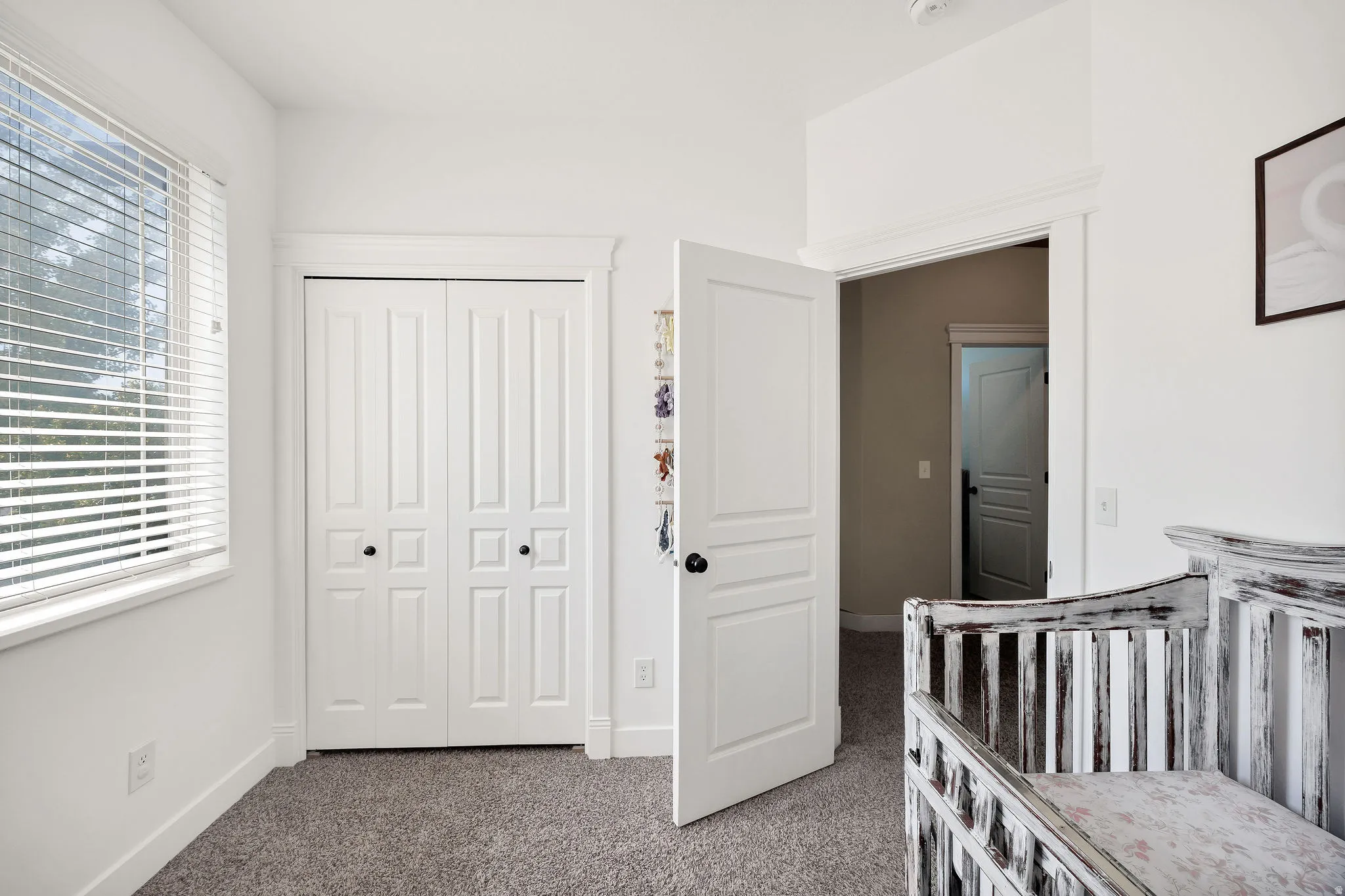 Room featuring a window with blinds, bi-fold closet doors, white trim, and light gray carpet