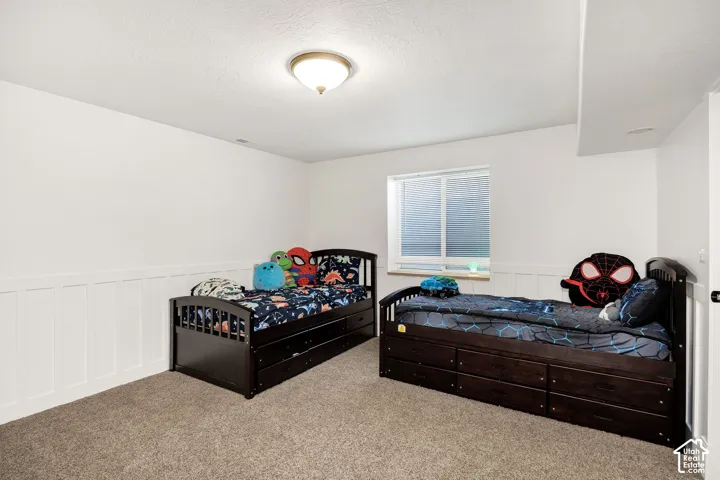 Spacious room featuring neutral carpet flooring, white walls with wainscoting, and a single window offering natural light
