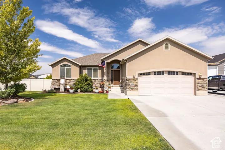 Contemporary stucco and stone-accented home featuring a two-car garage, concrete driveway, and a manicured front lawn