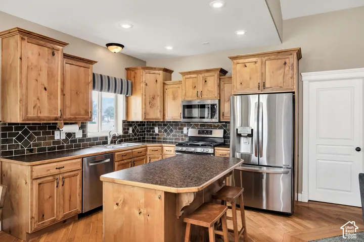Kitchen featuring knotty wood cabinetry, stainless steel appliances, a dark tile backsplash, a central island with a breakfast bar, and wood-finish flooring