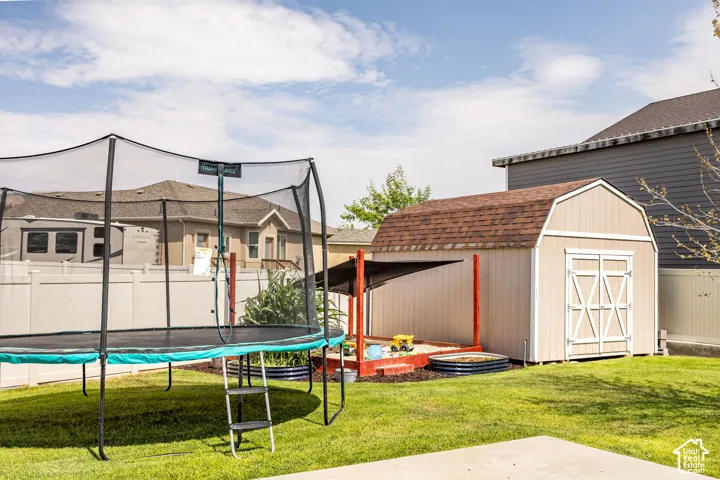 Expansive backyard featuring a spacious lawn, a charming storage shed with double barn doors and a shingled roof, a sandpit with a protective covering, and a privacy fence