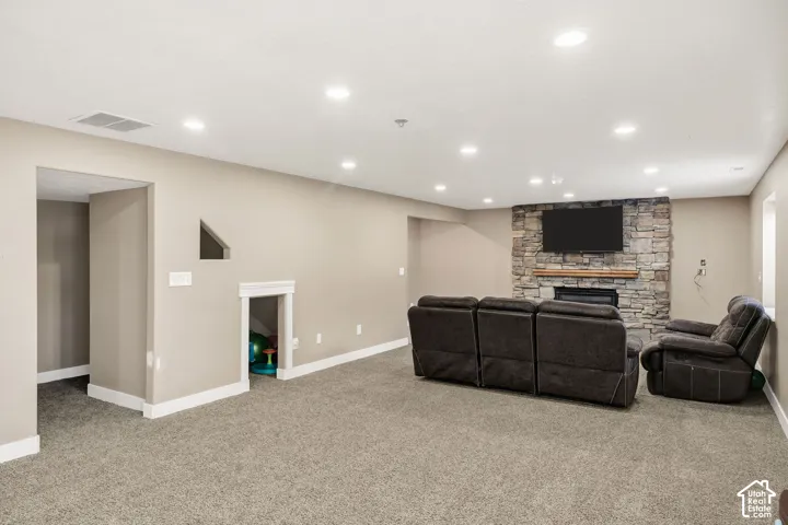 Spacious room featuring neutral carpeting, recessed lighting, and a stone-clad fireplace with a wood mantle