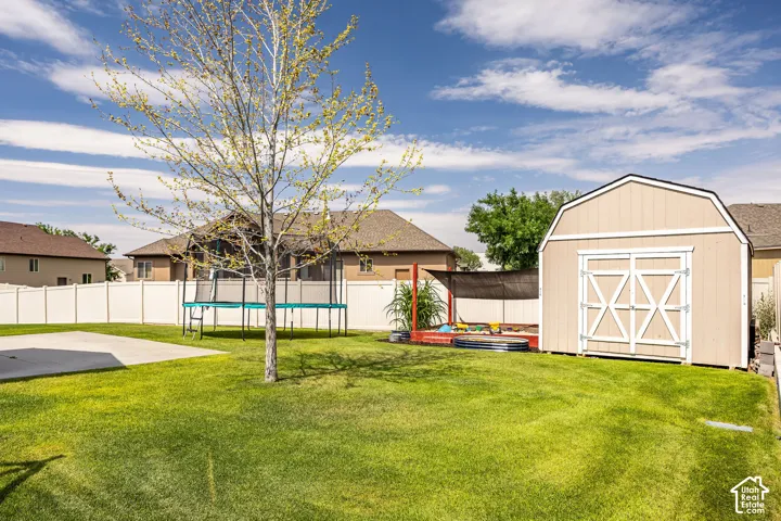 Expansive fenced backyard featuring a manicured lawn, concrete patio, and a dedicated storage shed