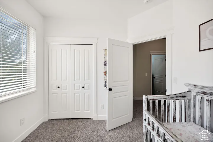 Room featuring a window with blinds, bi-fold closet doors, white trim, and light gray carpet