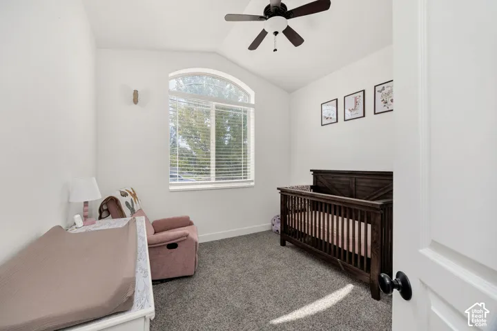 Room featuring a vaulted ceiling with a dark-toned ceiling fan and light fixture, a large arched window with blinds, and light gray carpet flooring