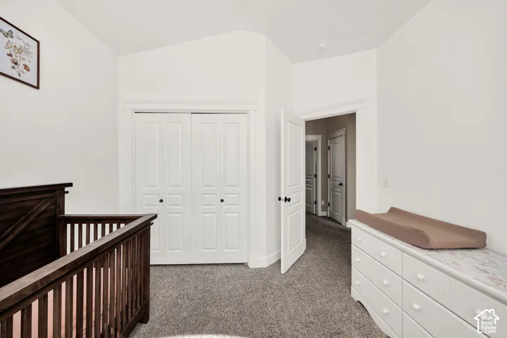 Vaulted ceiling room featuring light gray carpet, white bi-fold closet doors, and white interior doors with dark hardware