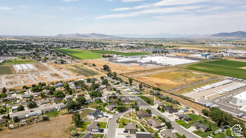 Aerial perspective of a residential street with single-family homes, surrounded by agricultural fields and commercial structures