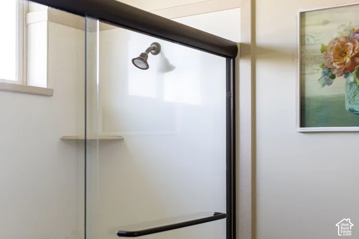 Walk-in shower featuring a bronze finish shower head, clear glass enclosure, and an integrated shelf