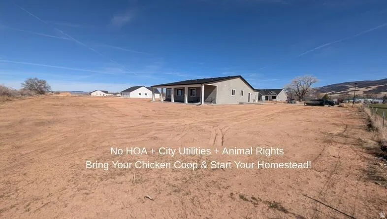 Expansive undeveloped land with a single-story residence featuring a covered patio, neutral stucco exterior, and dark roof