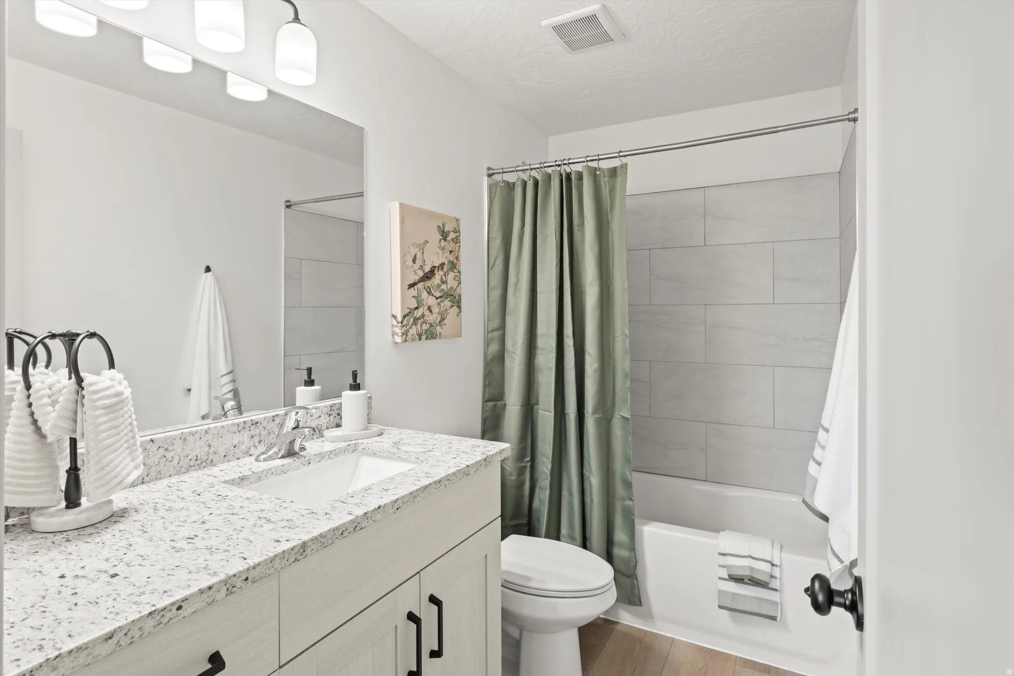 Modern bathroom featuring a single vanity with a white countertop and undermount sink, light wood-finish flooring, a full bathtub with light-colored subway tile surround, and a coordinating vanity mirror with overhead lighting