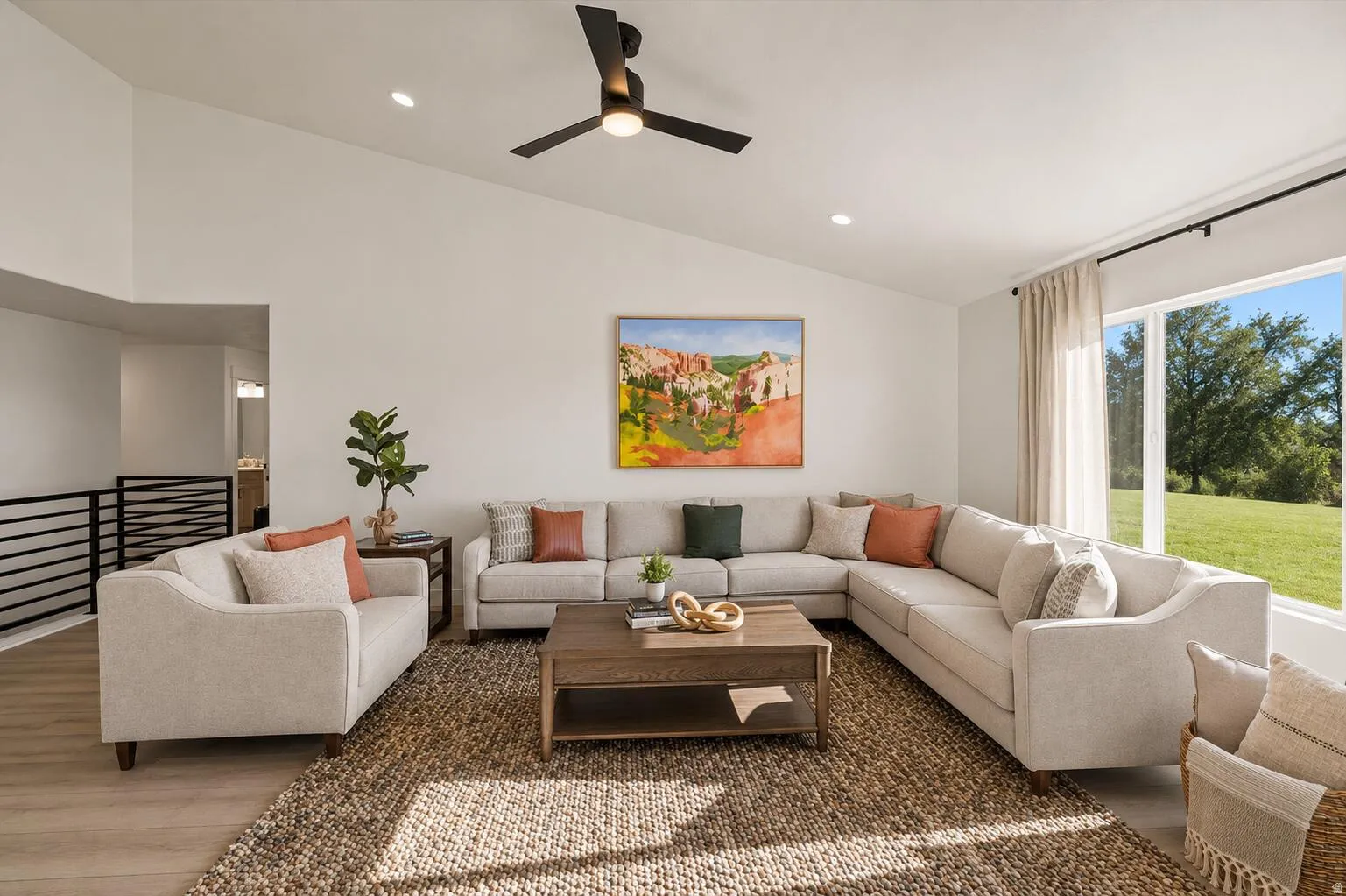 Spacious living area featuring a vaulted ceiling with recessed lighting and a ceiling fan, wood-finish flooring, a large window, and a black metal railing