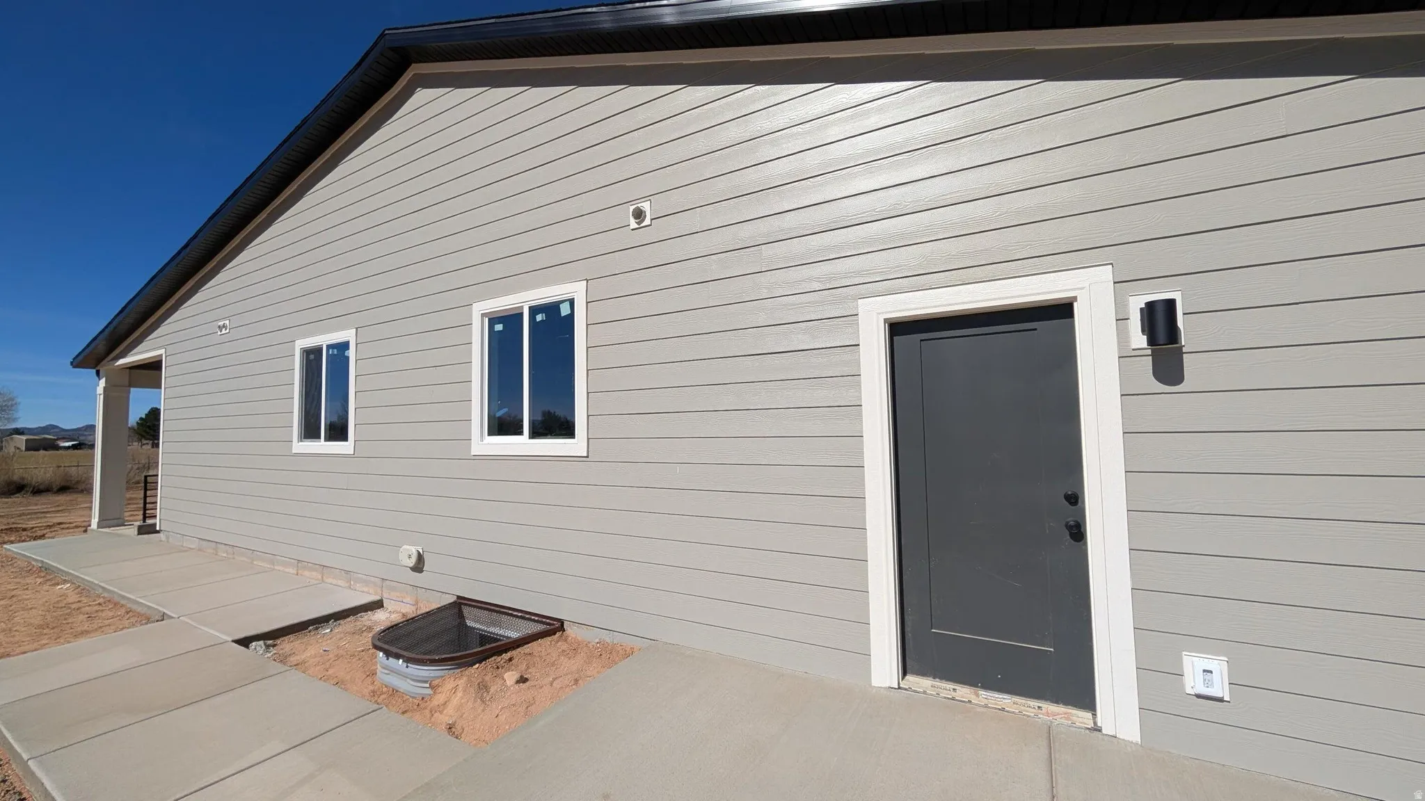 Light gray horizontal siding exterior with a dark gray door, white trim, and black exterior lighting