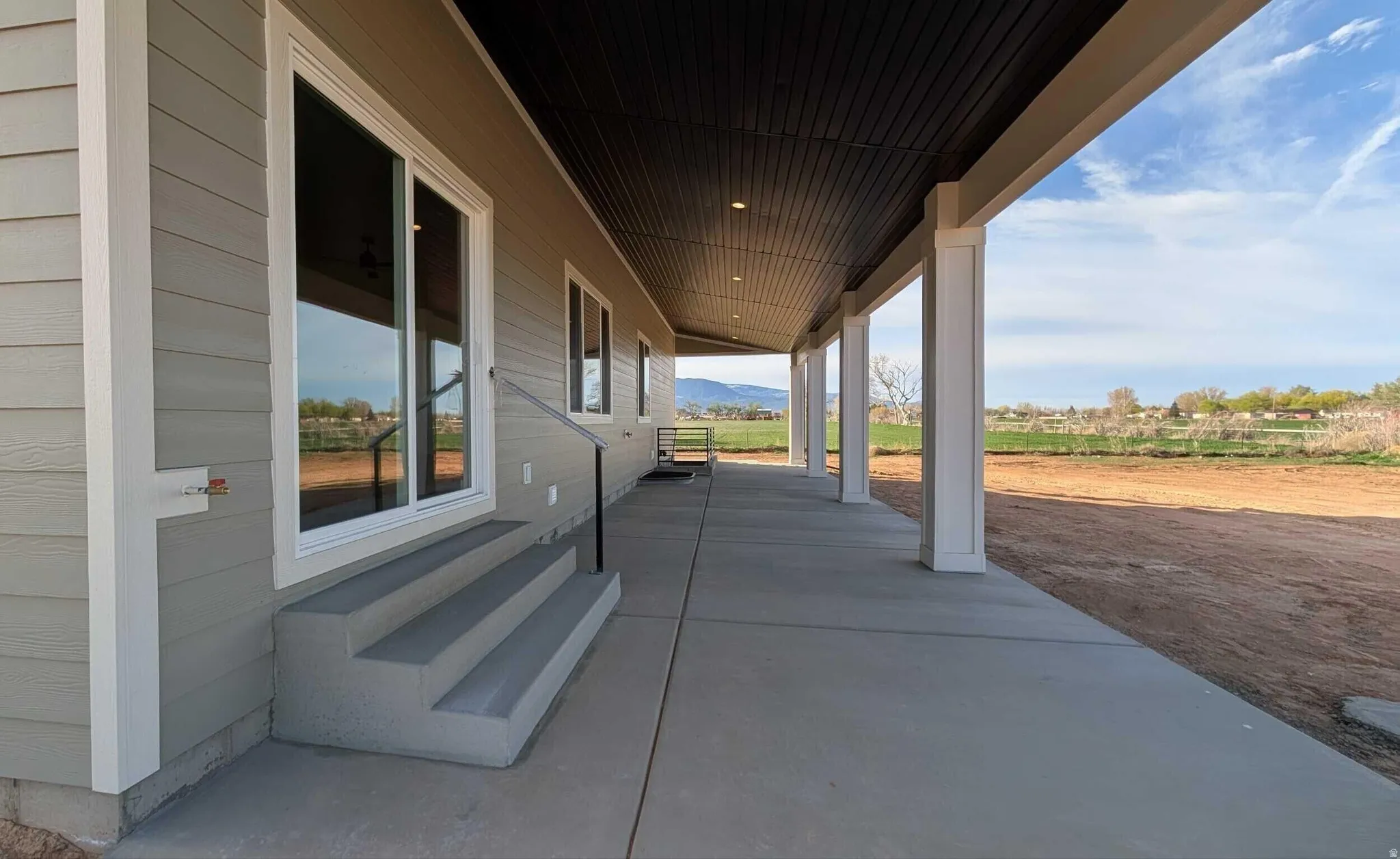 Expansive covered patio featuring a concrete surface, white support columns, and a dark wood-finish ceiling with recessed lighting