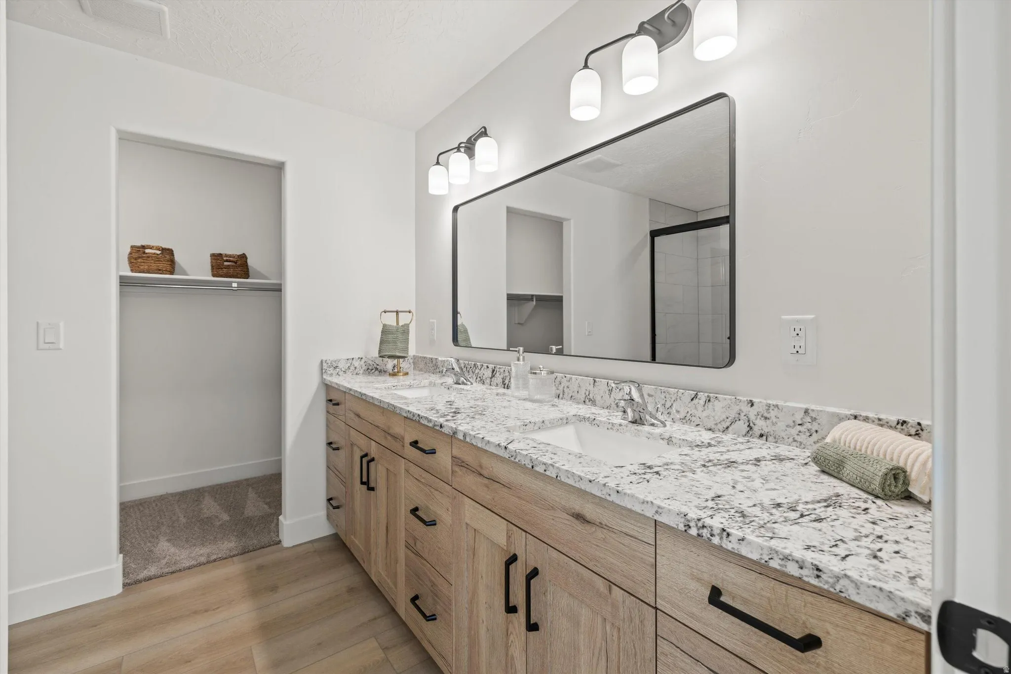 Double vanity with stone countertop, integrated sinks, wood-finish cabinetry, and matte black hardware