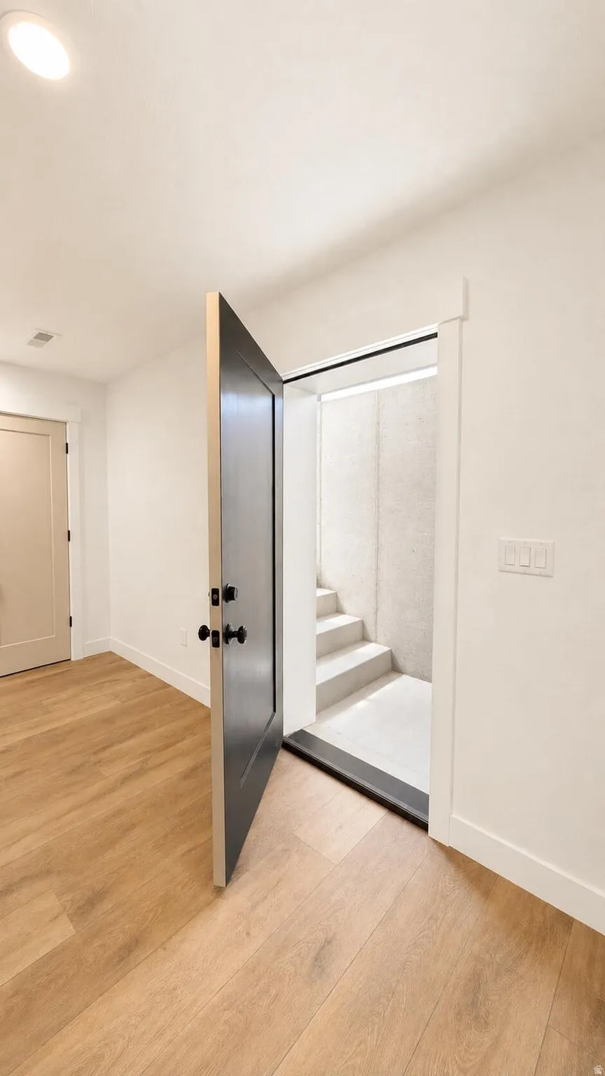 Interior entryway featuring light wood-finish flooring, white baseboards, and a black paneled door with matte black hardware