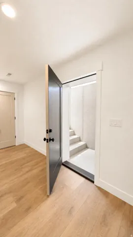 Interior entryway featuring light wood-finish flooring, white baseboards, and a black paneled door with matte black hardware