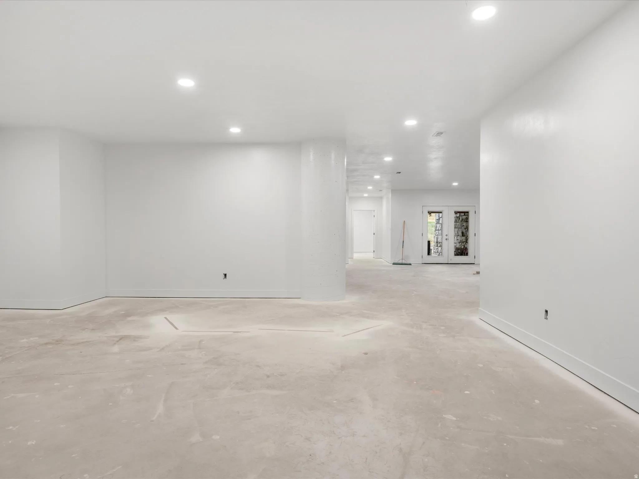 Spacious open-concept room with recessed lighting, white painted walls, and concrete flooring