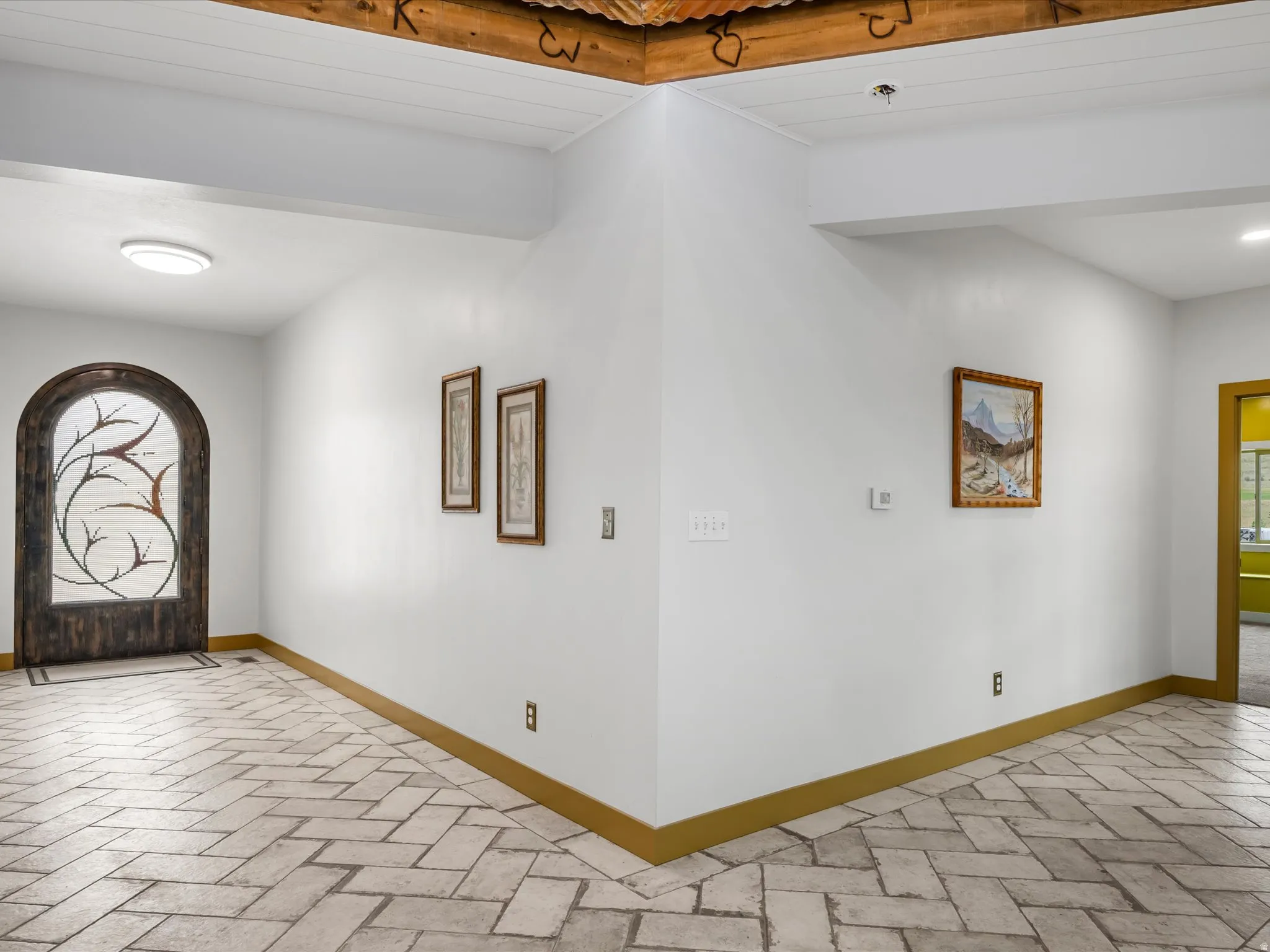 Entryway featuring herringbone-patterned tile flooring, an arched entry door with decorative glass, white walls with gold-toned trim, and a wood ceiling with corrugated metal accents