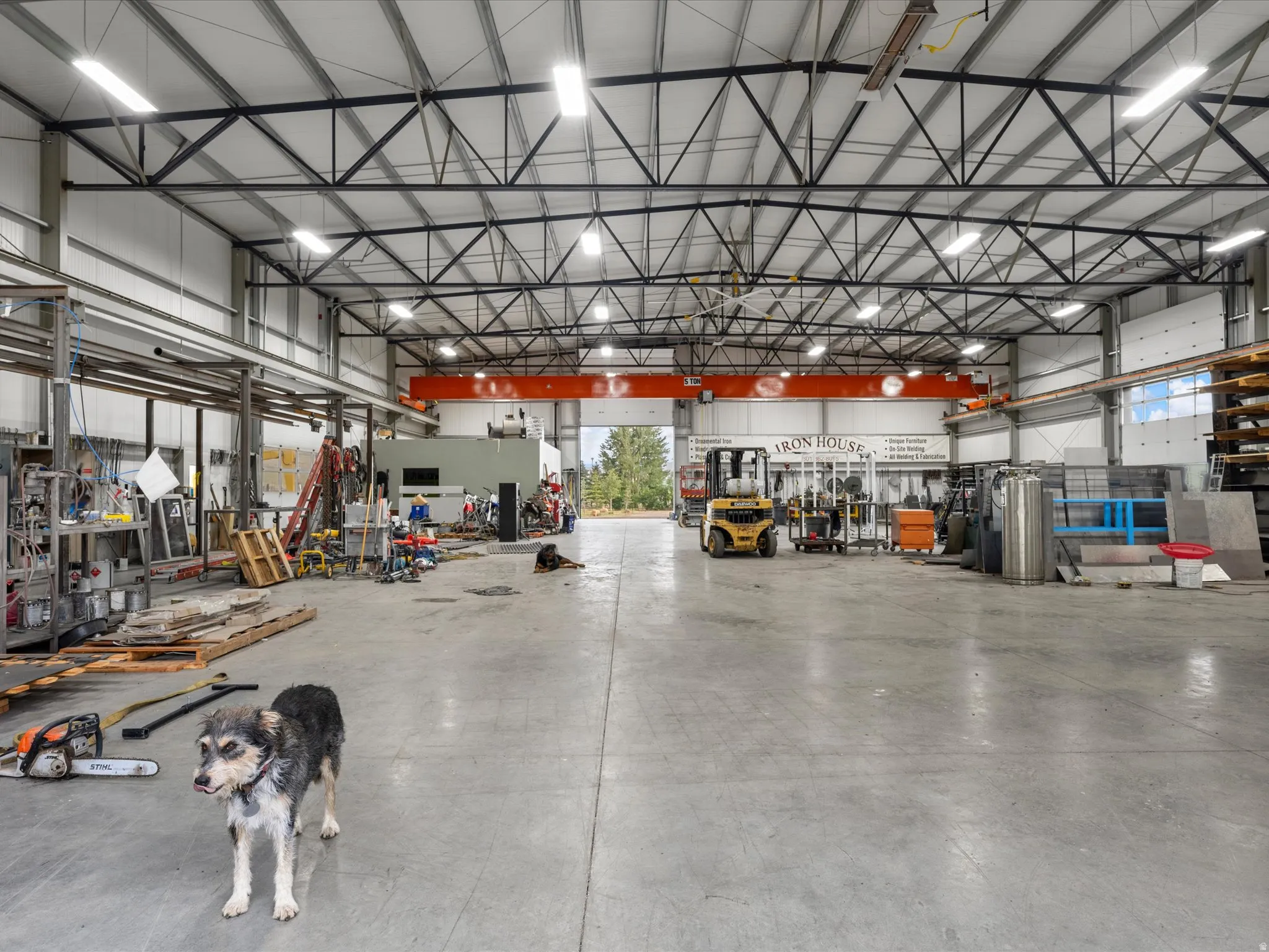 Spacious industrial interior featuring a high-clearance ceiling, concrete flooring, overhead crane system, and multiple roll-up doors