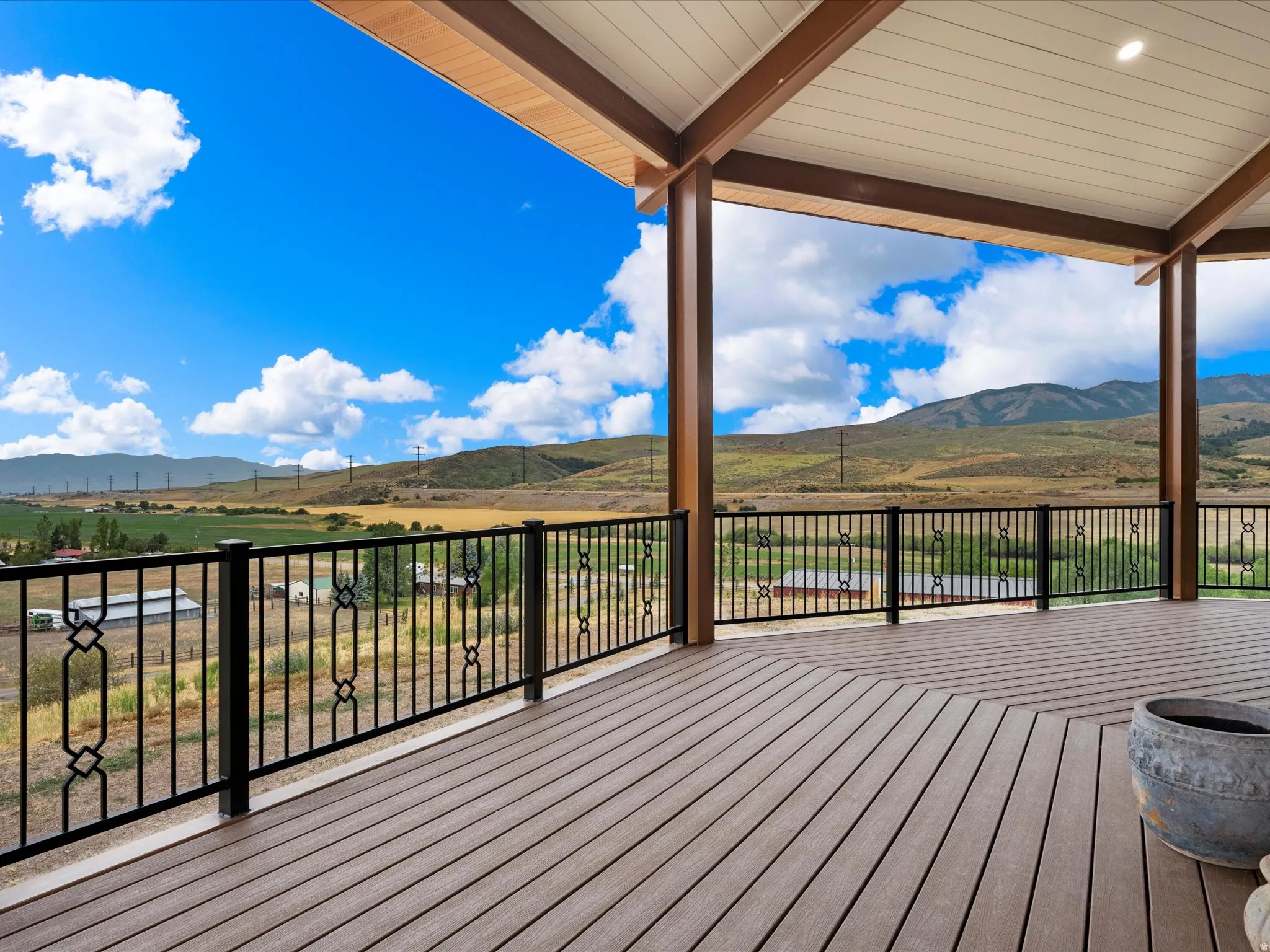 Expansive covered deck featuring wood-finish flooring, black wrought iron railing, exposed wood beams, and recessed lighting