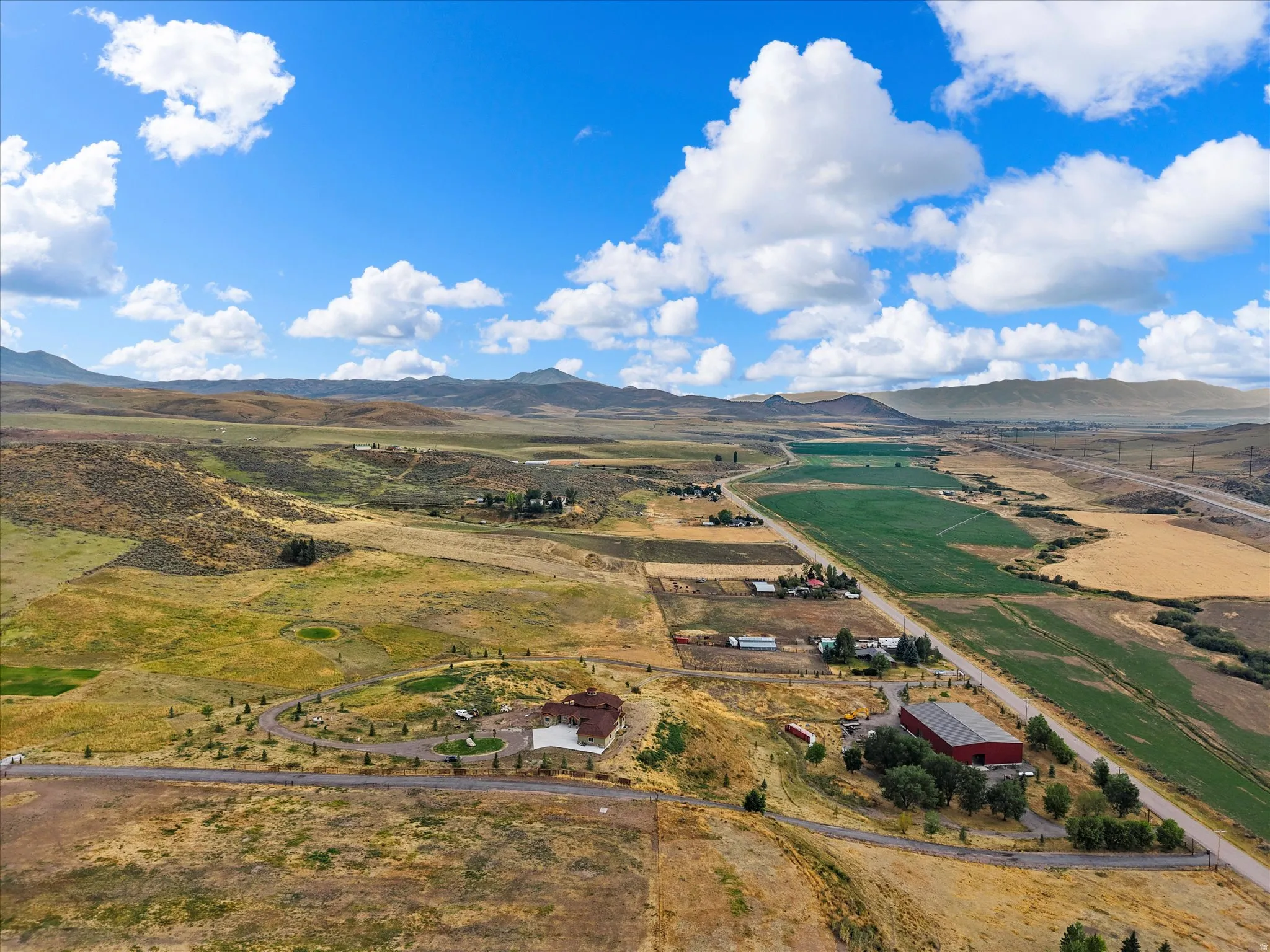 Expansive land parcel featuring a large residence with a circular driveway, a prominent red barn, and multiple agricultural fields